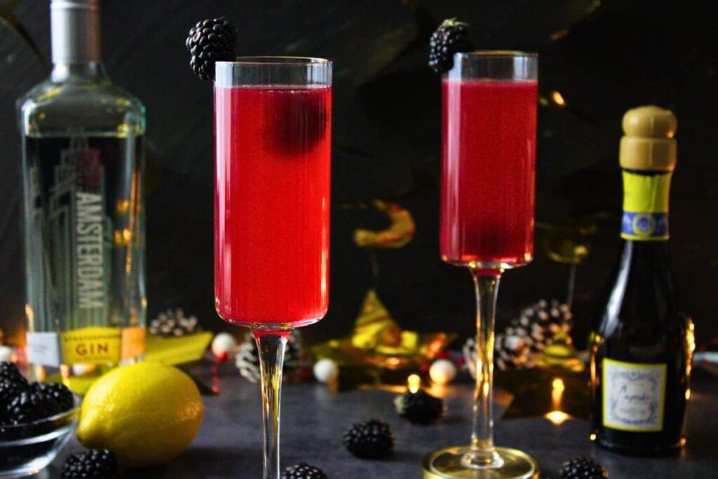 two blackberry french 75 drinks surrounded by alcohol bottles and gold decorations