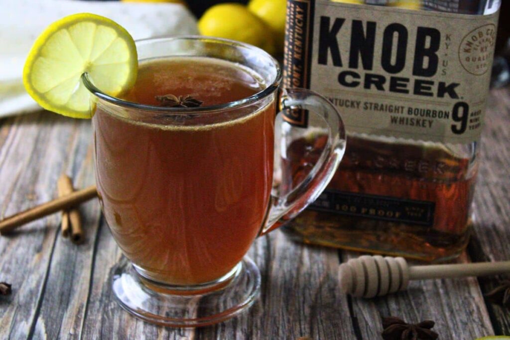 chai hot toddy with a slice of lemon next to bourbon bottle