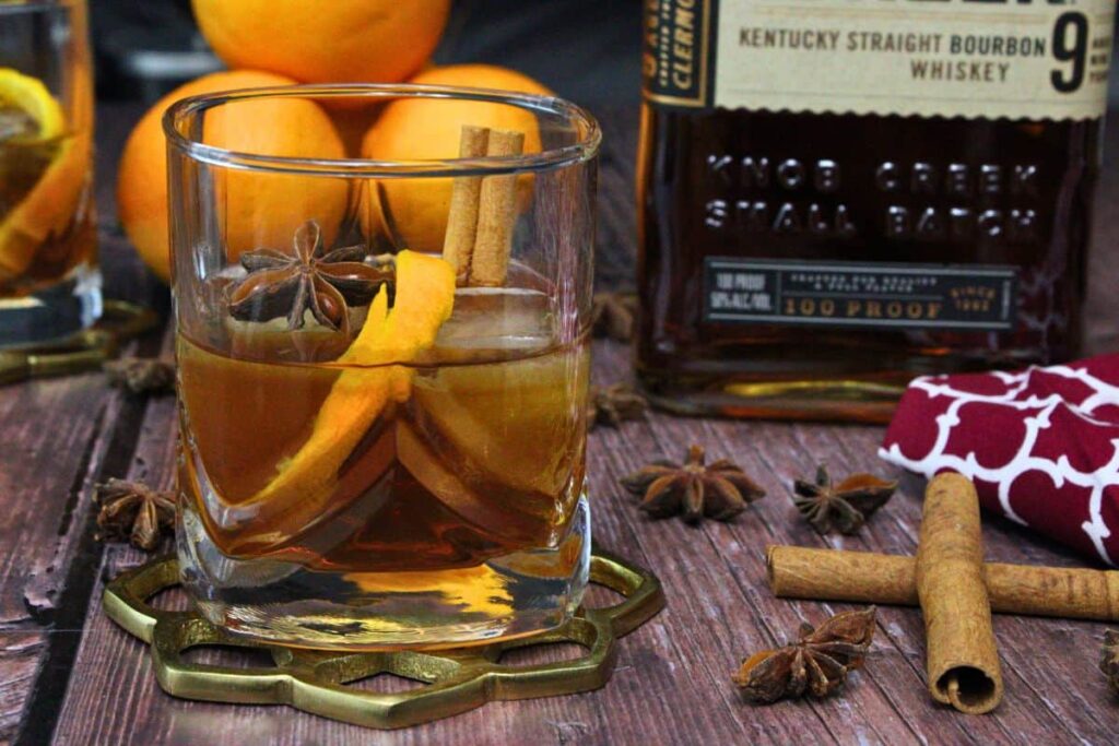 chai old fashioned with orange peel and cinnamon sticks next to bourbon whiskey bottle