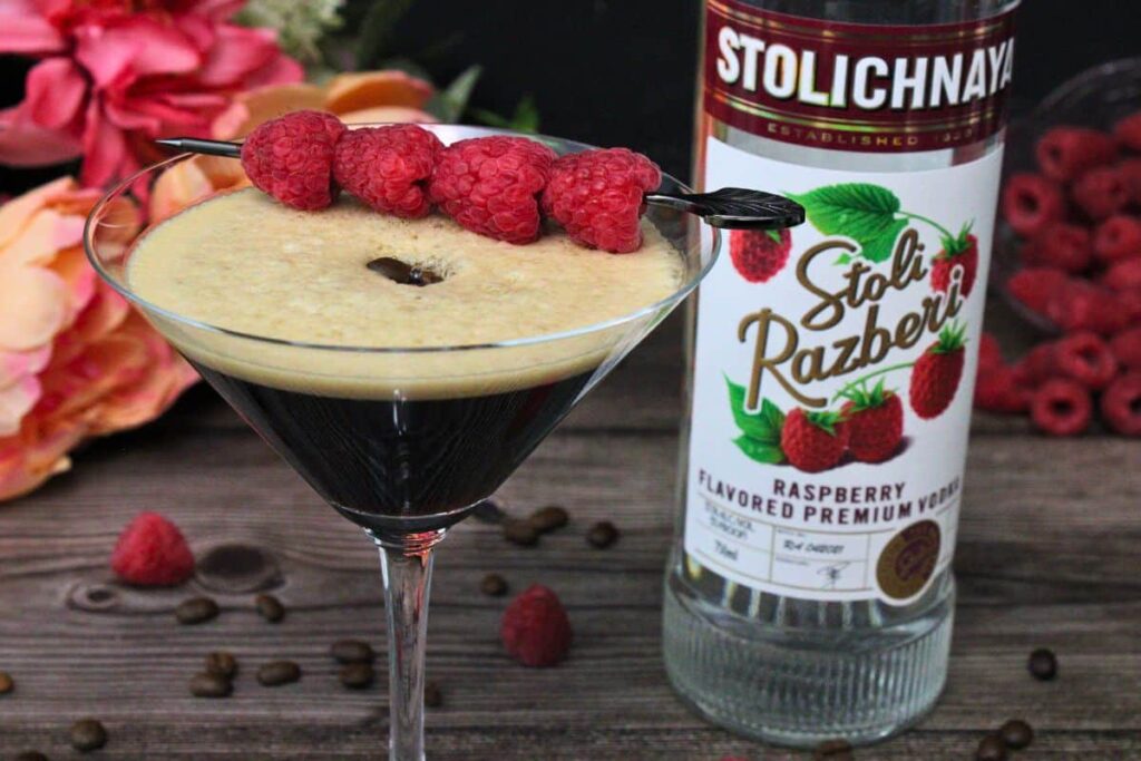 closeup of raspberry espresso martini with raspberry skewers next to vodka bottle