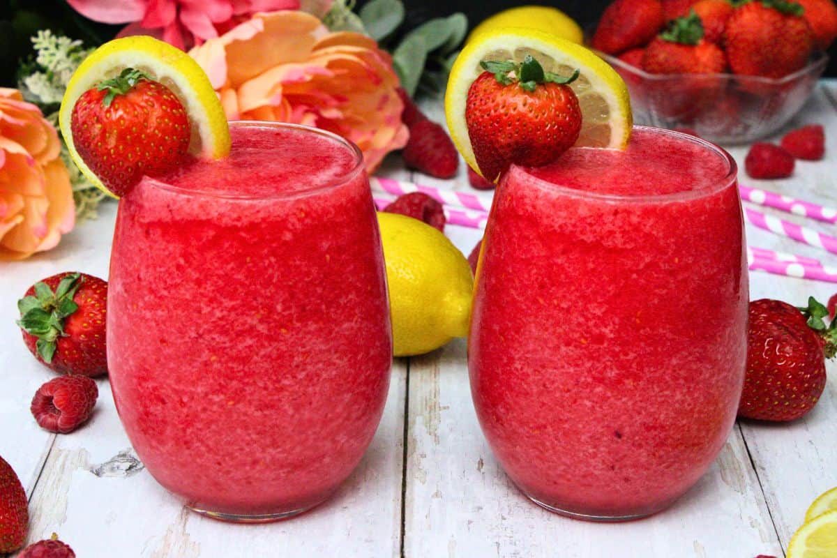 two pink whitney slushie drinks garnished with lemon and strawberry