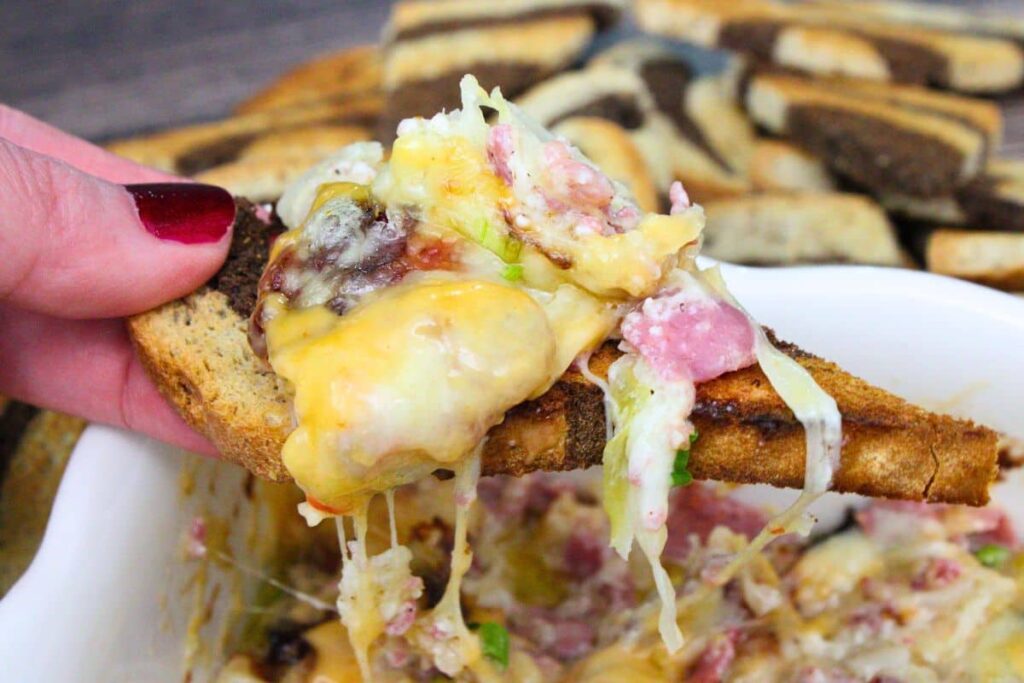 holding up a piece of toasted rye bread topped with air fryer reuben dip