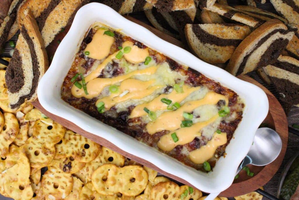 overhead view of reuben dipped topped with thousand island dressing surrounded by pretzel crackers and toasted rye bread pieces