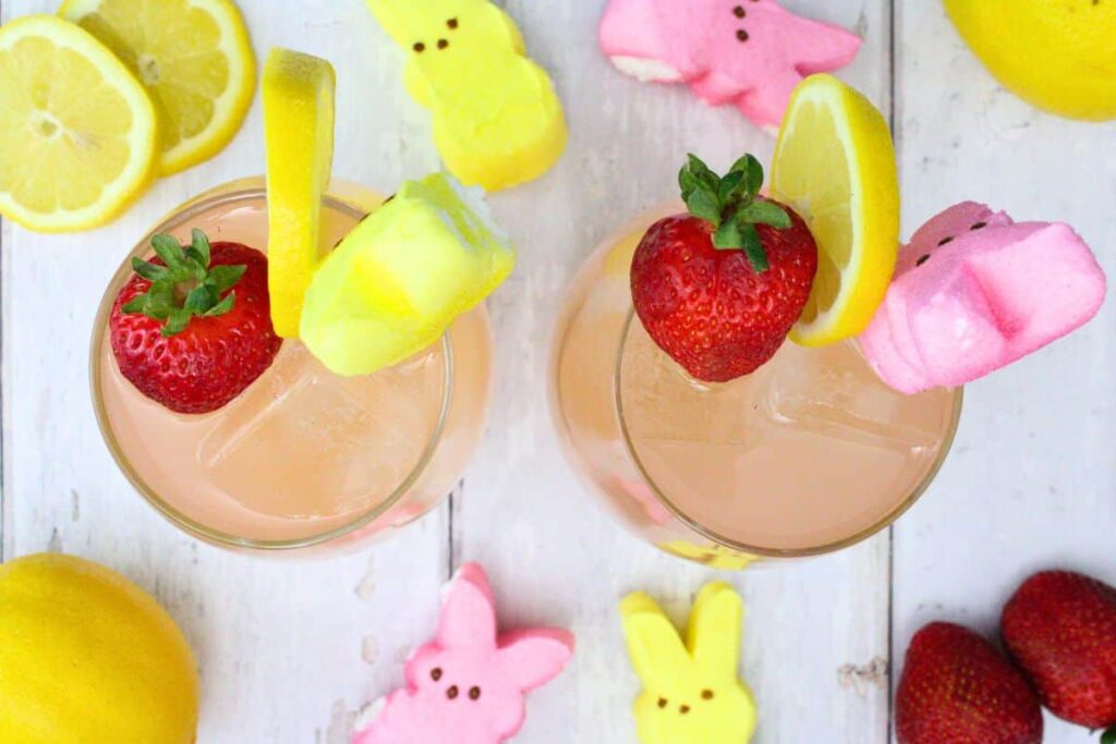 overhead view of two drunk bunny drinks garnished with marshmallow peeps, lemon, and strawberry on a white wooden table