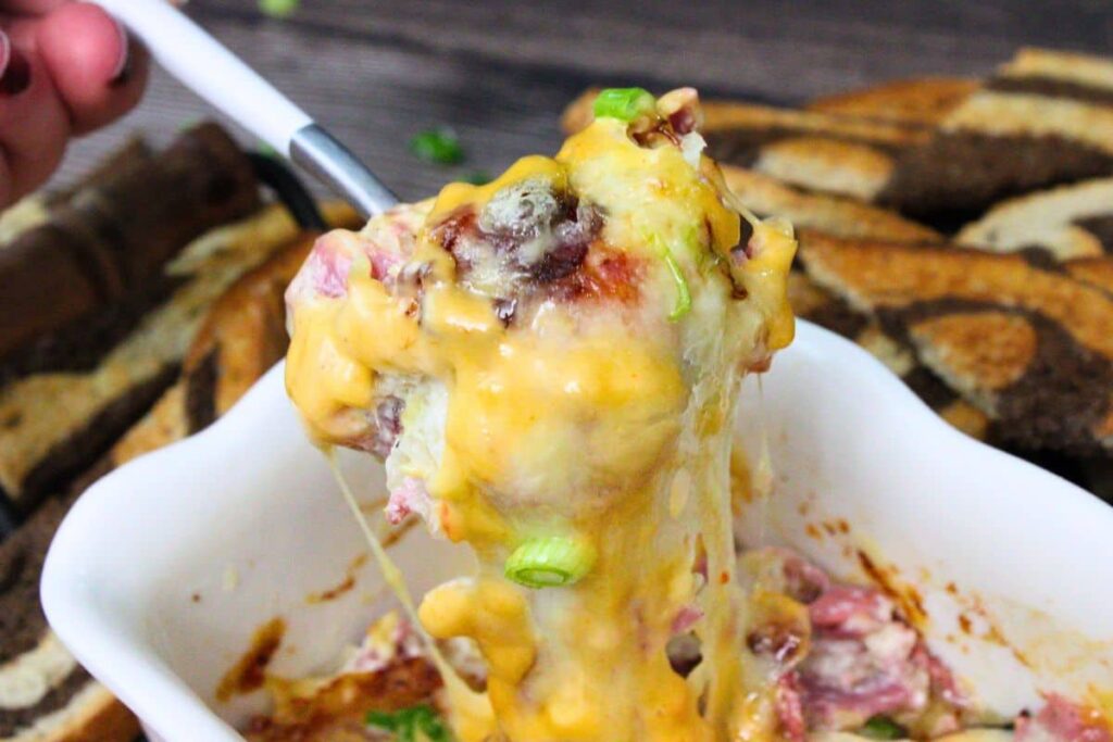 scooping up air fryer reuben dip on a spoon showing the thousand island dressing, melty cheese, sauerkraut, and corned beef