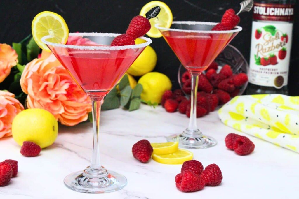 two raspberry lemon drops garnished with fresh fruit on a white counter