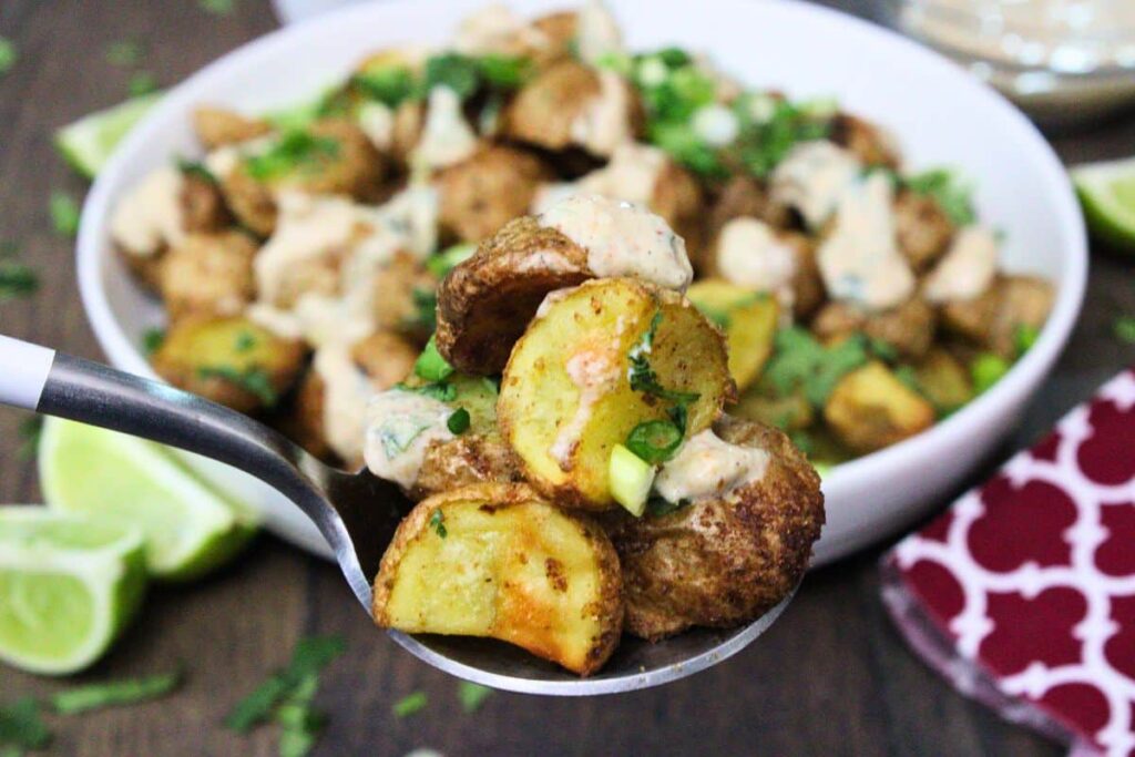 holding up a spoonful of gunpowder potatoes with a drizzle of yogurt raita