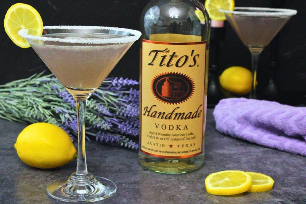 lavender lemon drop martini with a lemon slice next to vodka bottle