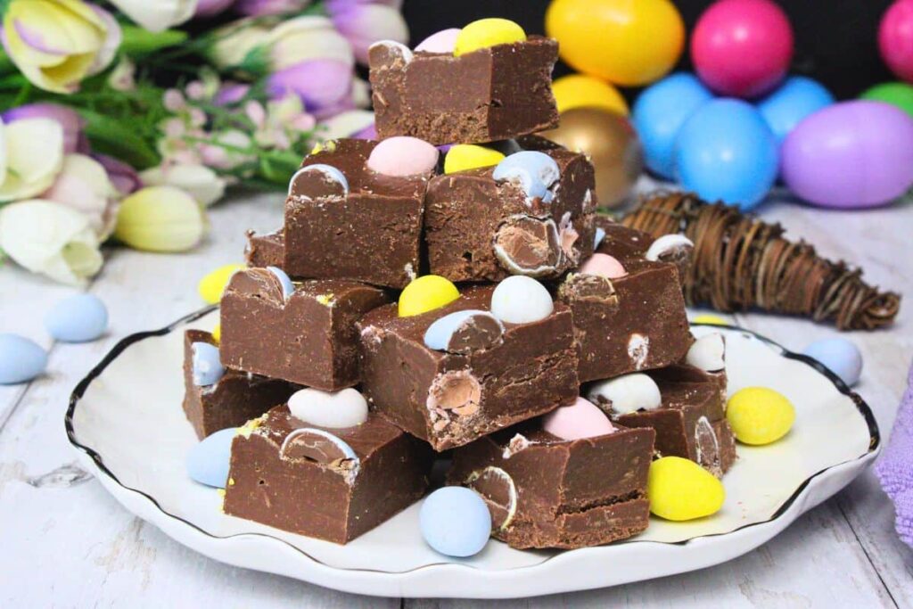 mini egg fudge stacked up on a plate in front of easter eggs and flowers