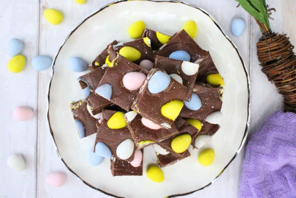 overhead view of mini egg fudge stacked on a plate surrounded by mini candy eggs