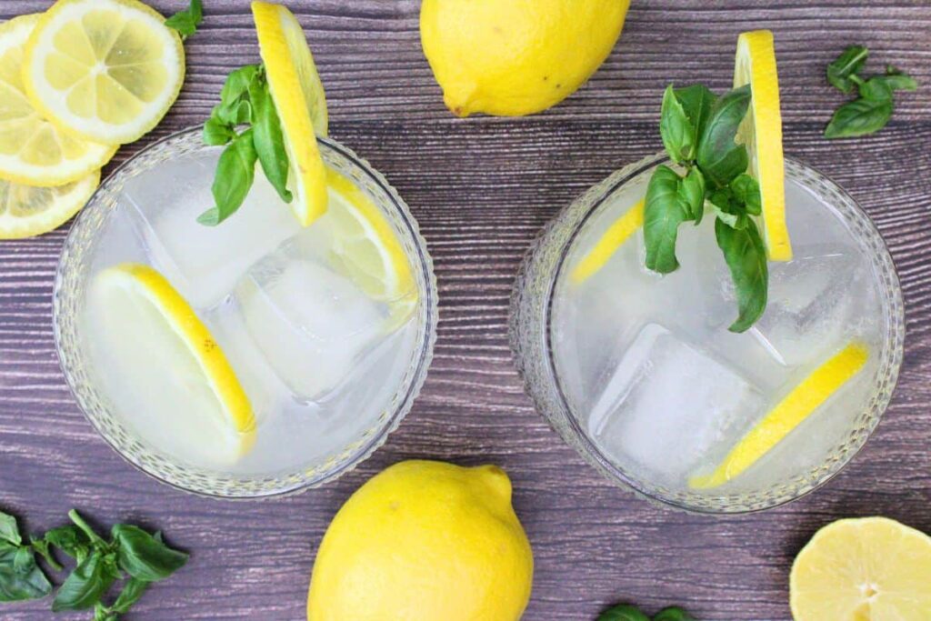 overhead view of two lemonade vodka punch drinks garnished with lemon and basil on a wooden table