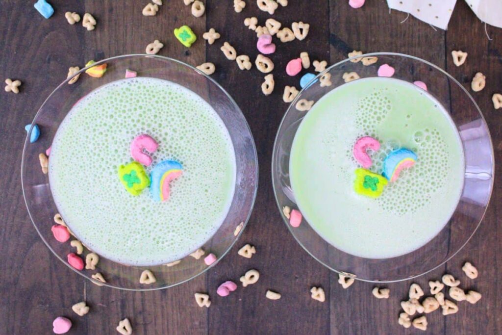 overhead view of two lucky charms martini cocktails with three marshmallows each surrounded by cereal pieces