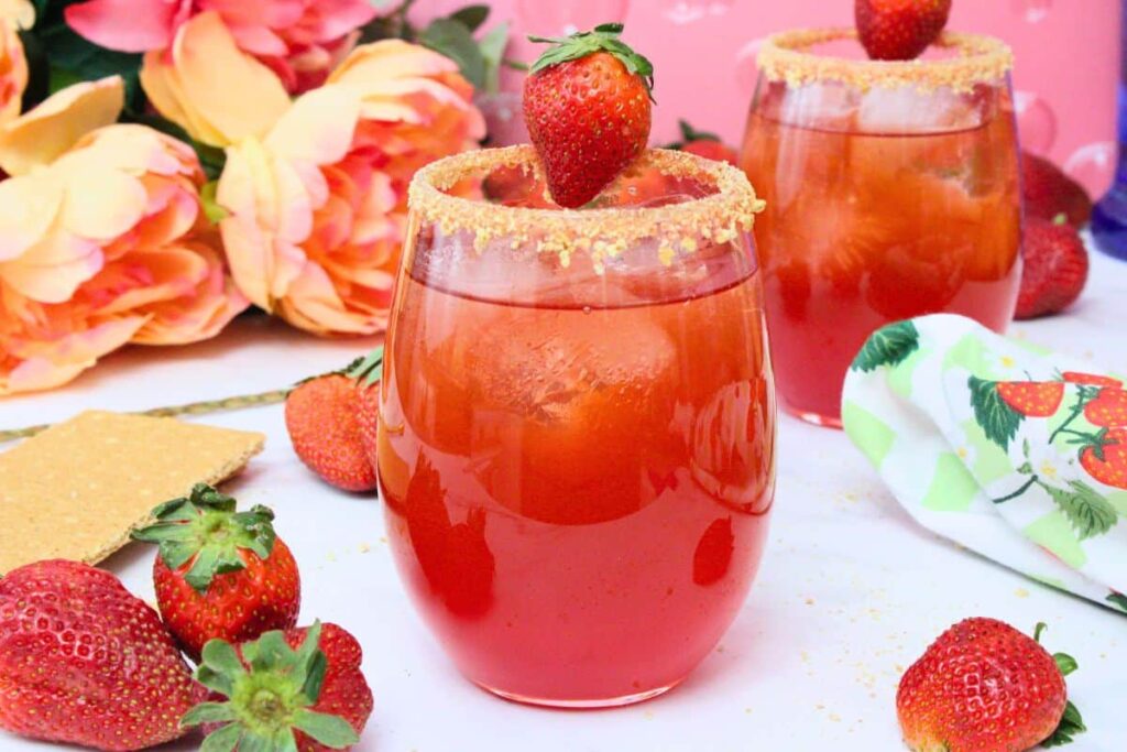 strawberry shortcake cocktail with a graham cracker crust rim surrounded by fresh berries and light flowery decor