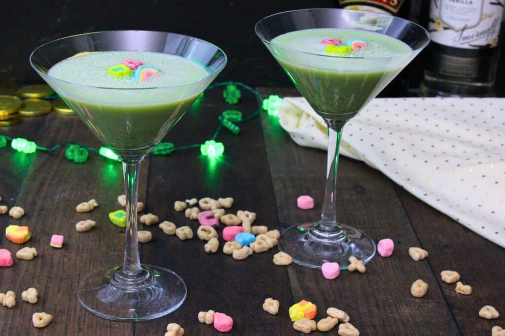 two lucky charms martinis on a wooden table surrounded by lucky charms cereal pieces