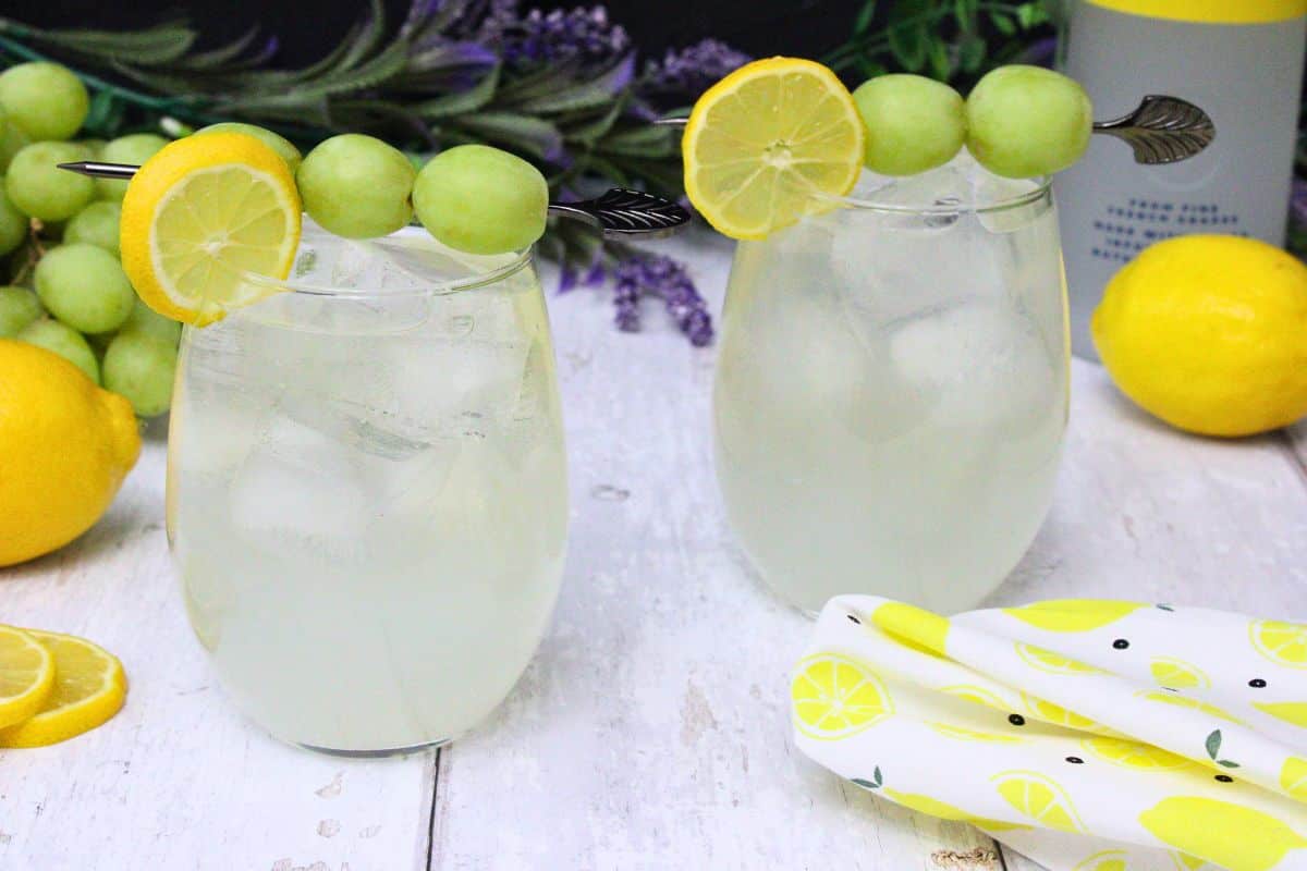 two vodka lemonade spritzers garnished with lemon and grape on a white wooden table
