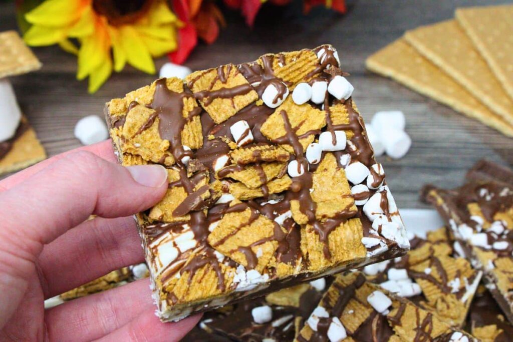 holding up a square of smores bark showing off golden grahams and mini marshmallows
