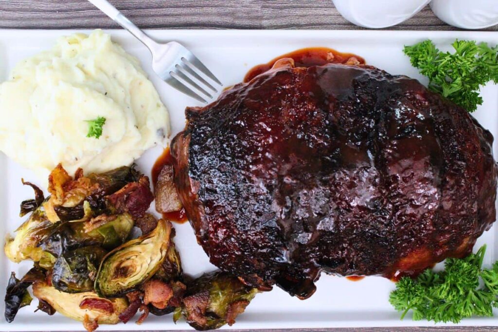 overhead view of bacon wrapped meatloaf on a platter with mashed potatoes and bacon brussel sprouts