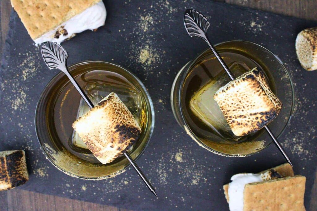 overhead view of two smores old fashioned drinks with a toasted marshmallow skewer