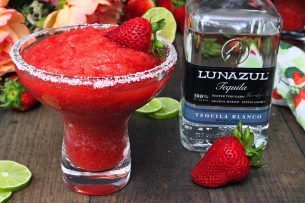 frozen strawberry margarita with salt rim and fresh strawberry next to tequila bottle