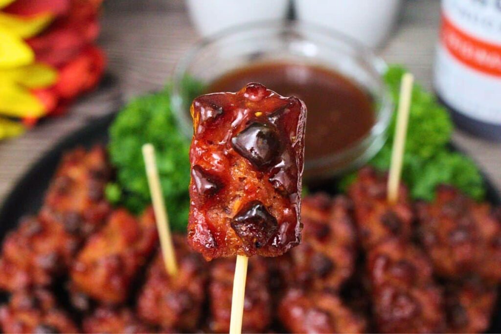 holding up an air fryer hot dog pinecone on a toothpick dipped in bbq sauce