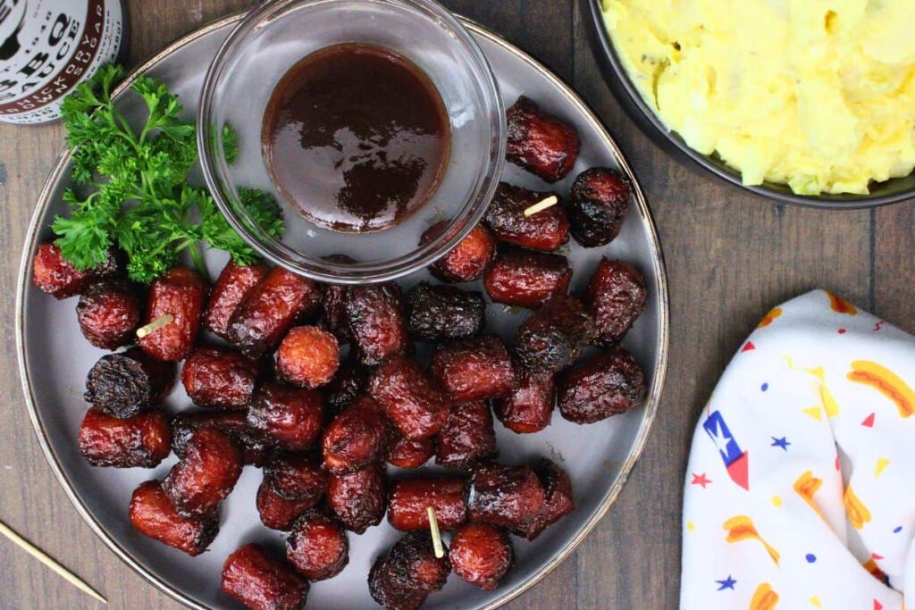 overhead view of hot dog burnt ends on a plate with bbq sauce and a side of potato salad