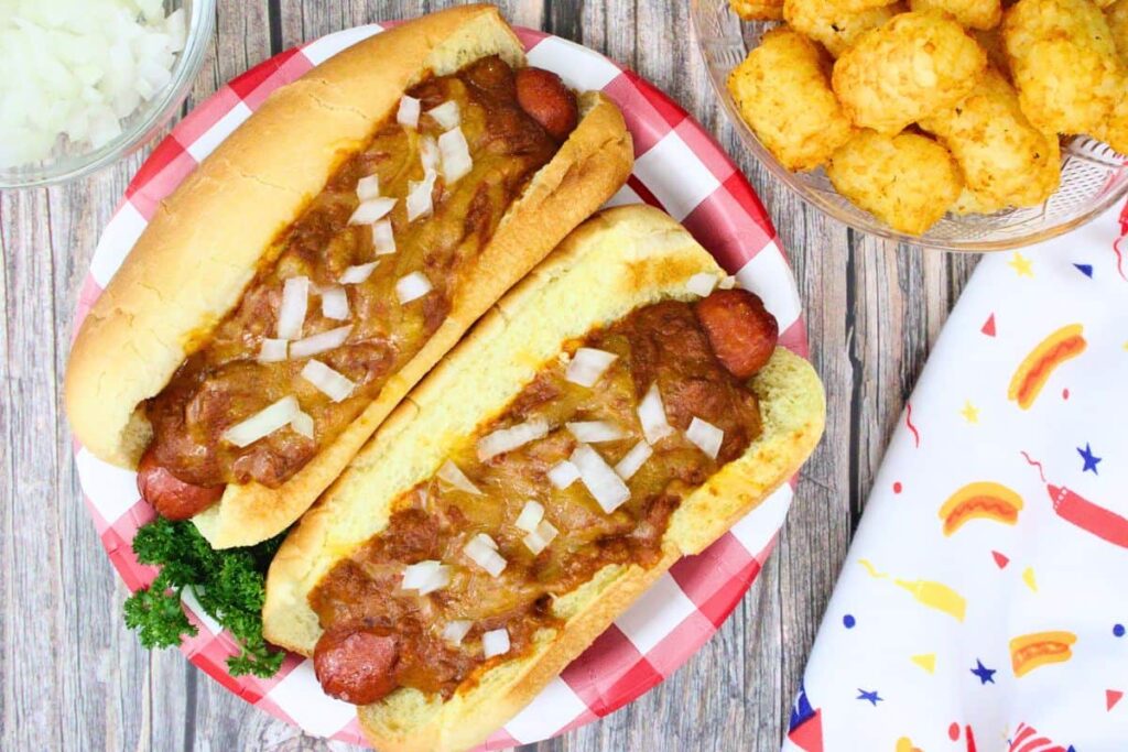 overhead view of two sonic chili cheese dogs topped with onions on a plate next to tater tots and a summer napkin