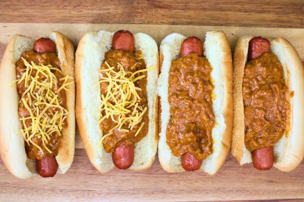 top heated hot dogs with chili sauce and shredded cheese