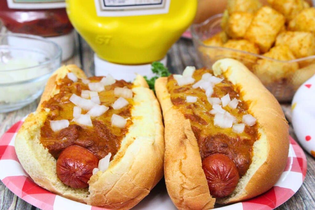 two sonic chili cheese dogs topped with onions side by side in front of ketchup, mustard, and tater tots