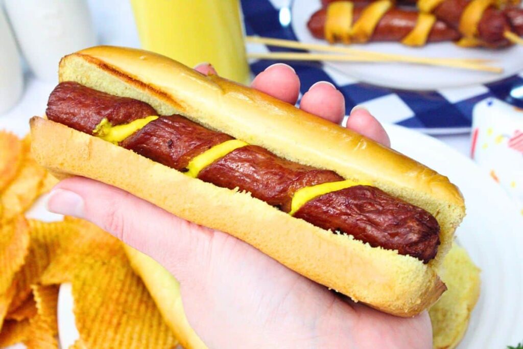 holding a spiral hot dog made in the air fryer with mustard laying in the spiral grooves