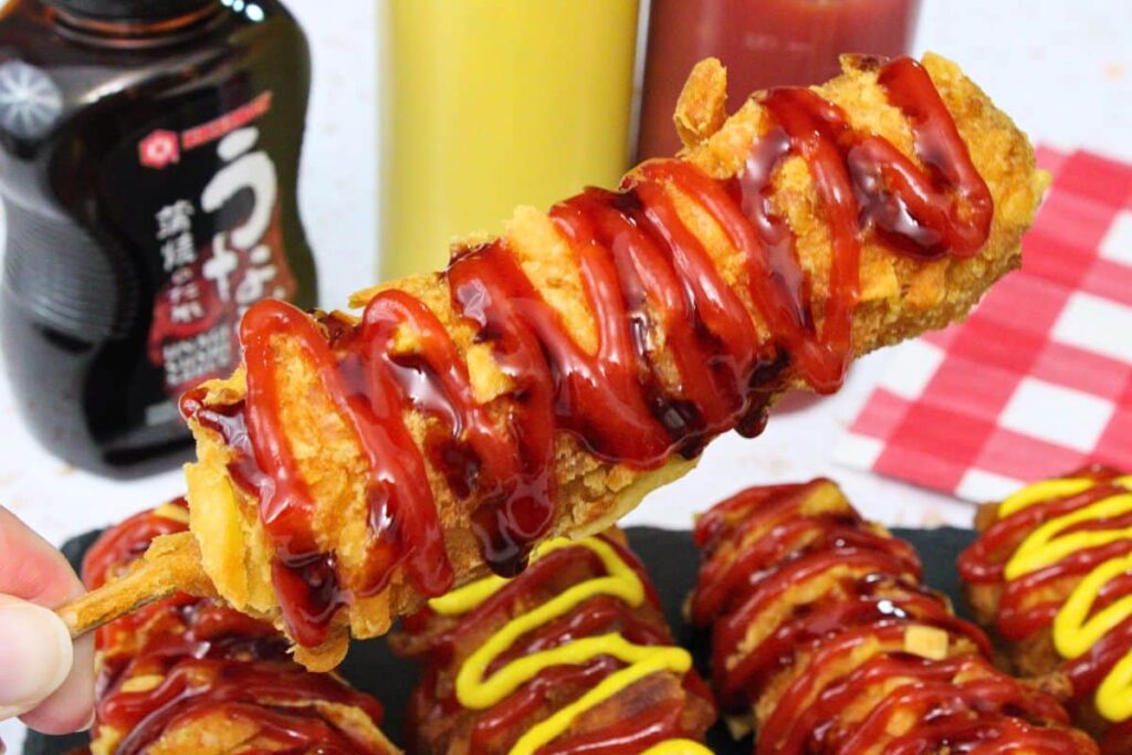 holding up and air fryer frozen korean corn dog with swirls of ketchup and sushi sauce