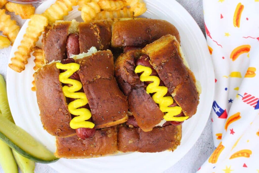 overhead view of hot dog sliders with a mustard swirl on a plate with crinkle cut french fries