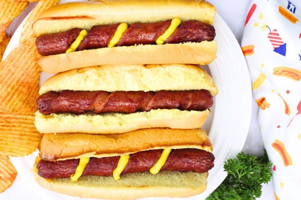 overhead view of three spiral hot dogs in buns laid vertically with mustard in the spiral cuts