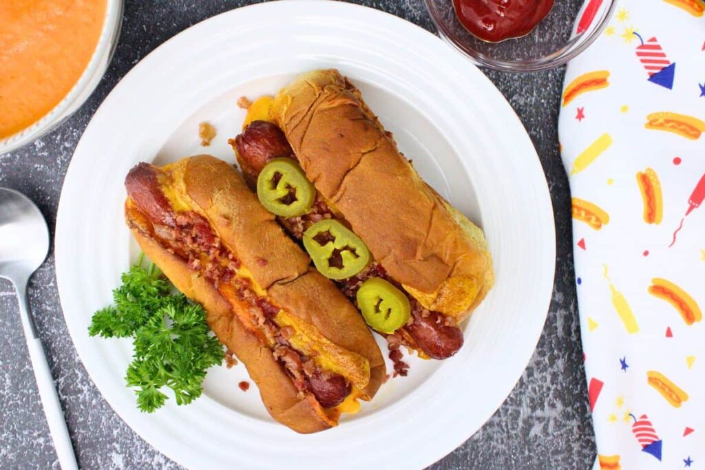 overhead view of two grill cheese hot dogs topped with bacon bits and jalapenos