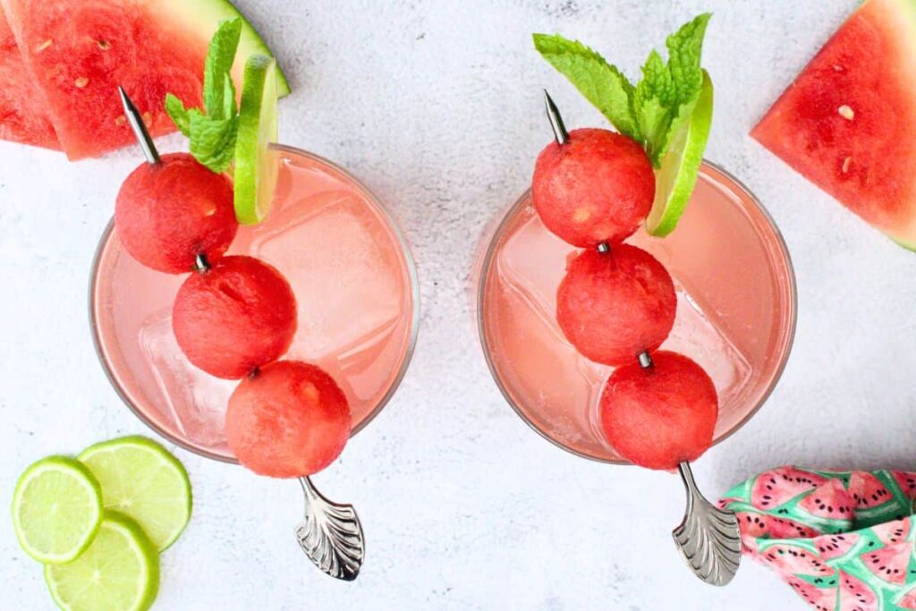overhead view of two watermelon gin fizz drinks with three melon ball skewer, mint, and fresh lime