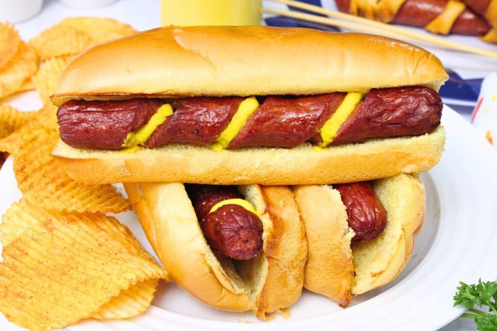 three spiral hot dogs stacked on a white plate with the top on showing mustard in the spiral cuts