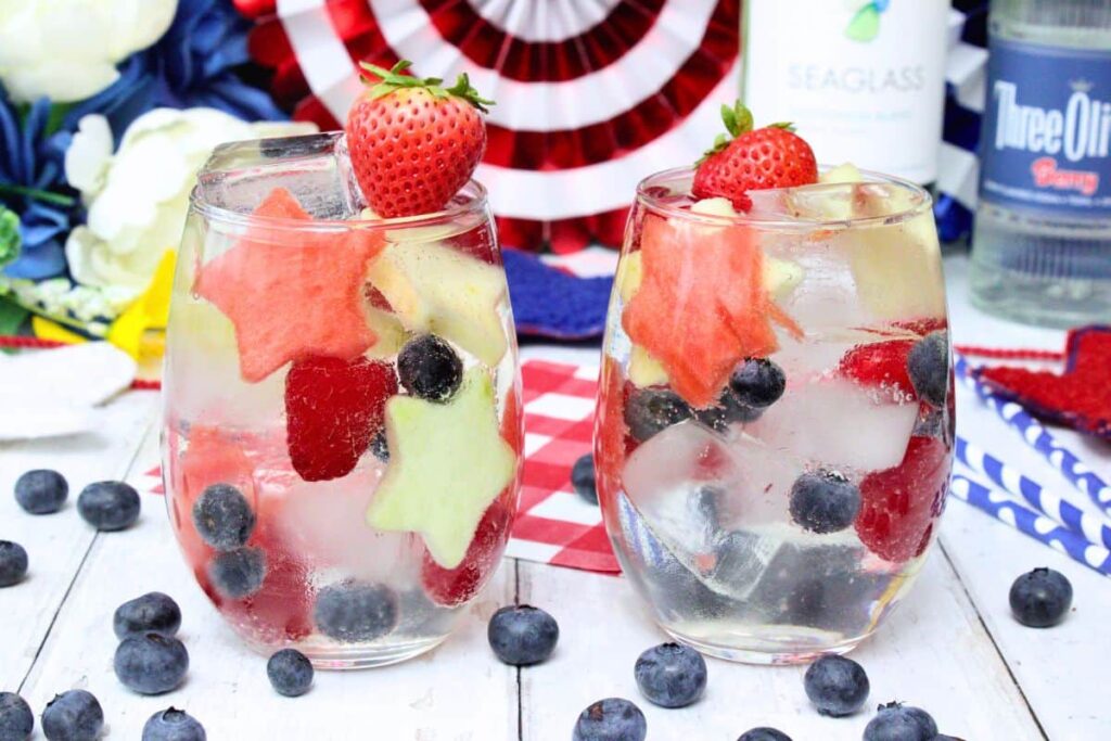 two glasses of red white and blue sangria filled with fresh fruit and blueberries surrounding