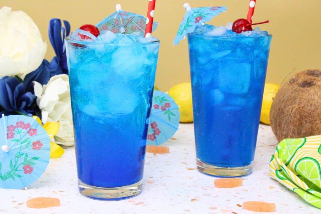 two sonic ocean water drinks side by side with a maraschino cherry and straw amidst tropical background
