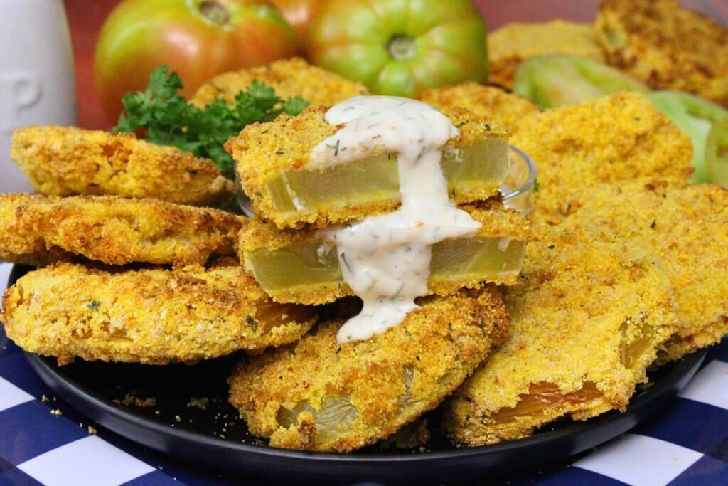 closeup view of air fryer fried green tomatoes on a plate with one cut in half dripping with hot honey ranch