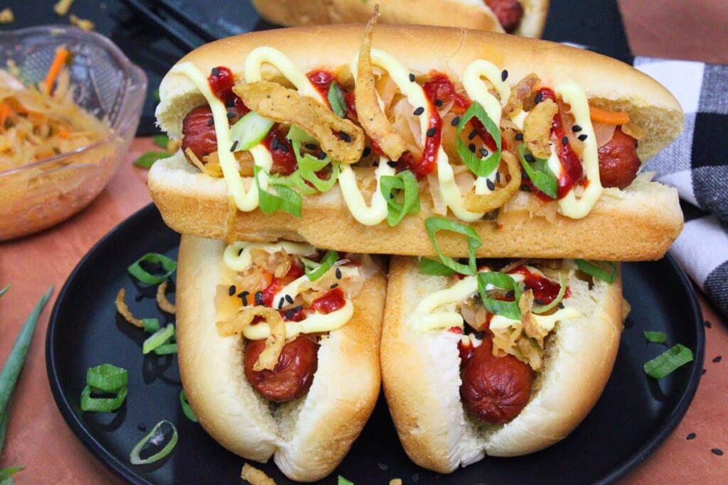 closeup view of three kimchi hot dogs with kewpie mayo stacked up on a black plate