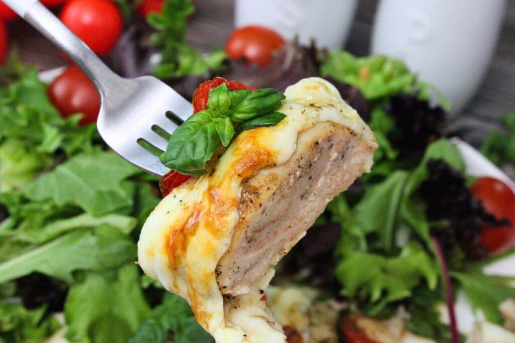 holding up a fork with a piece of juicy air fryer hasselback chicken topped with mozzarella and tomato
