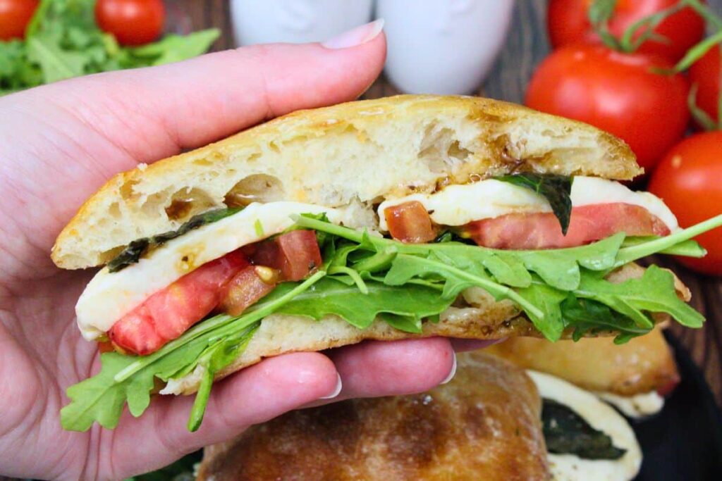 holding up half of an air fryer caprese sandwich showing off the tomato, mozzarella cheese, and arugula