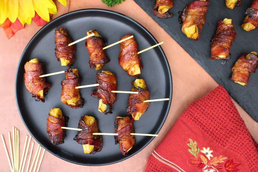 overhead view of bacon wrapped apples with toothpicks on a black plate