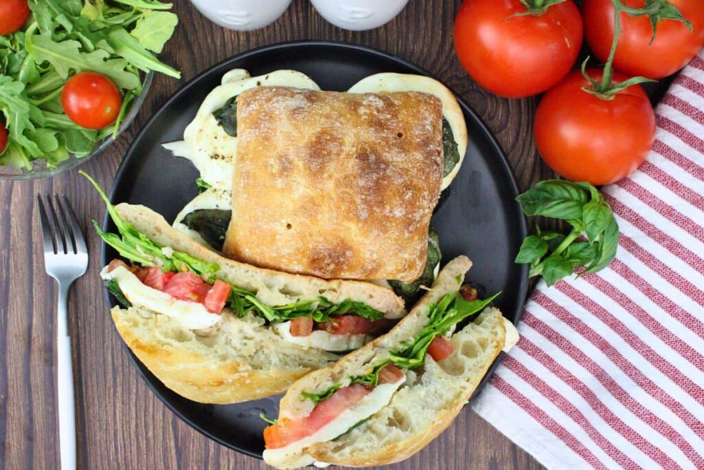 overhead view of two air fryer caprese sandwiches on a black plate showing off the fresh ingredients and melty cheese
