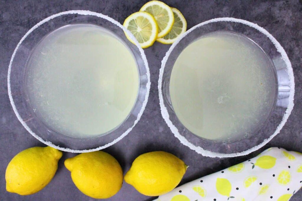 overhead view of two lemon drop martinis on a dark counter with fresh lemons