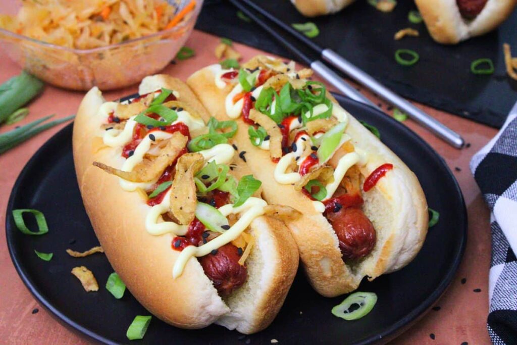 two air fryer kimchi hot dogs with kewpie mayo and chopped green onions on a black plate