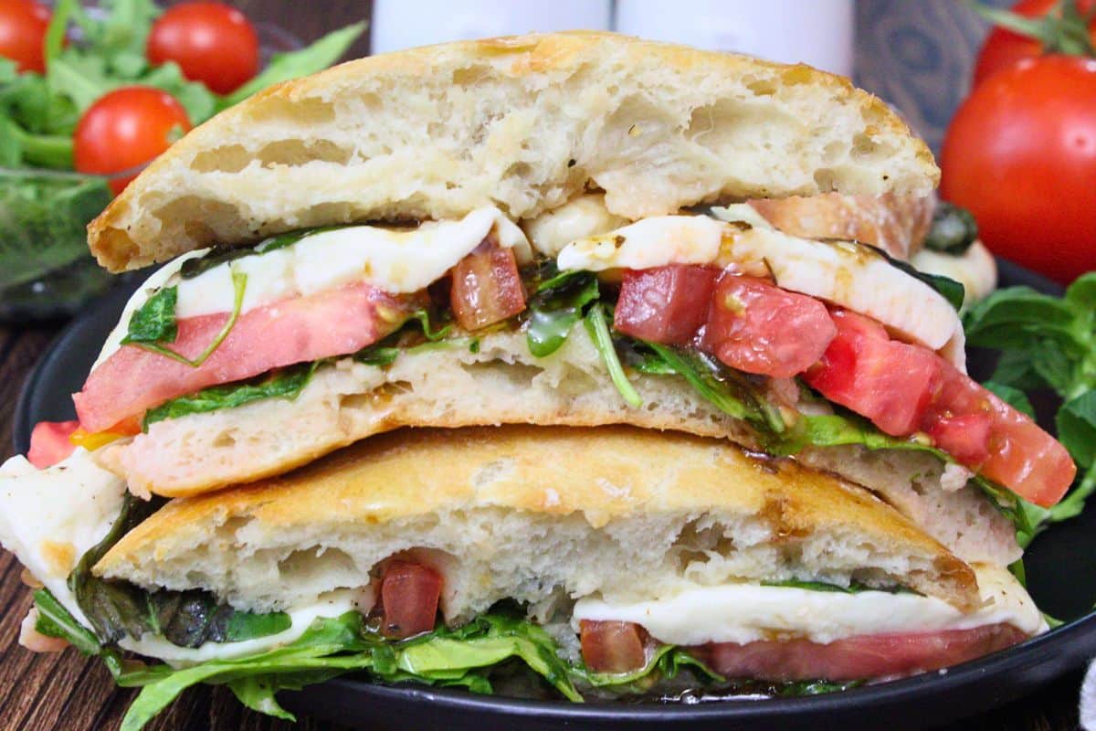 two halves of caprese sandwich stacked on top of each other showing tomatoes mozzarella cheese and fresh greens