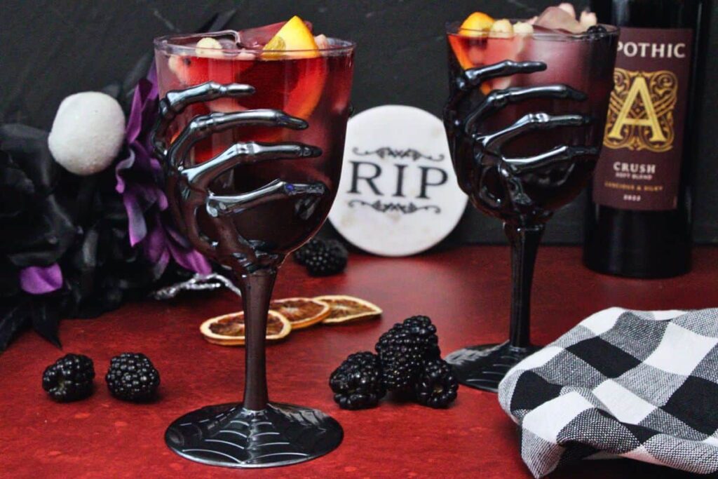 two skeleton hand goblets filled with halloween sangria showcasing ghost shaped apple slices and orange