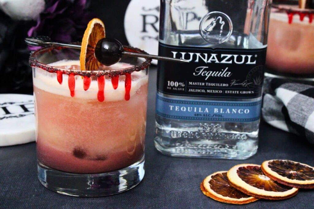 closeup of bloody tequila sunset garnished with a skewer of blood orange and cherry