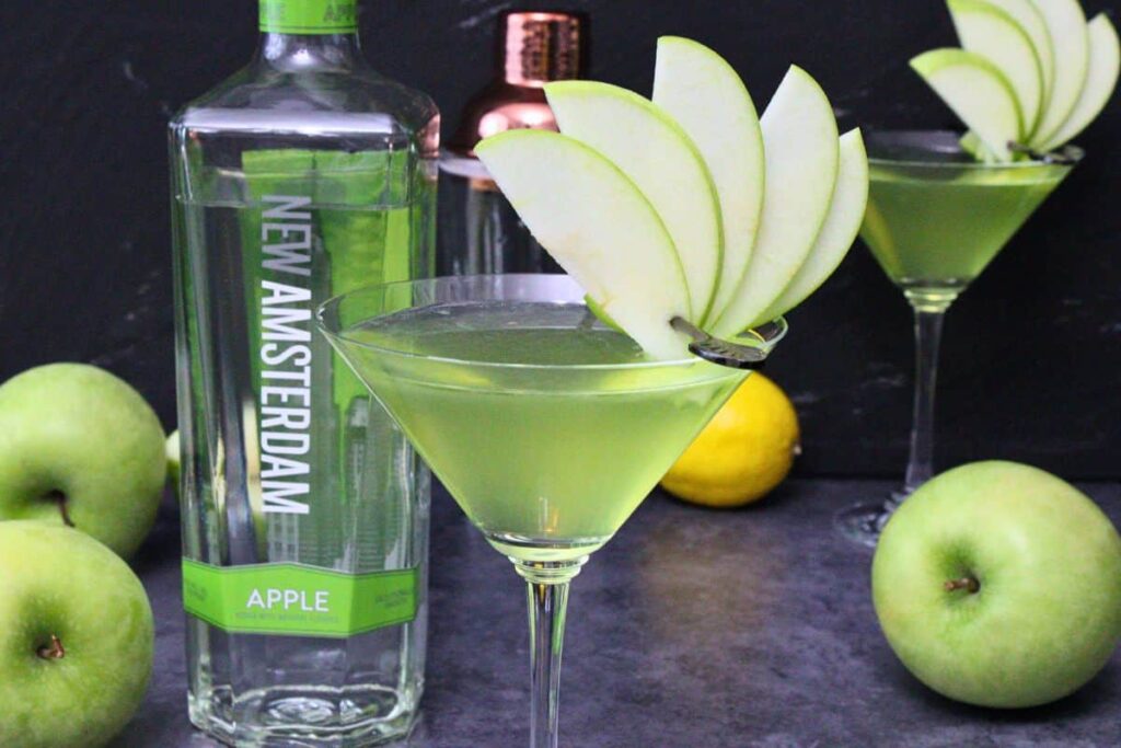 closeup view of appletini with fresh apple skewer fan in front of liquor bottles