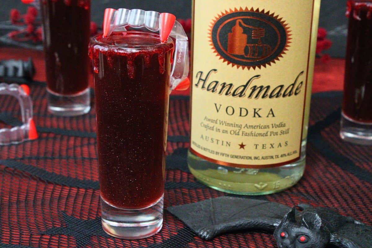 closeup view of vampire bite shot topped with vampire fangs next to vodka bottle